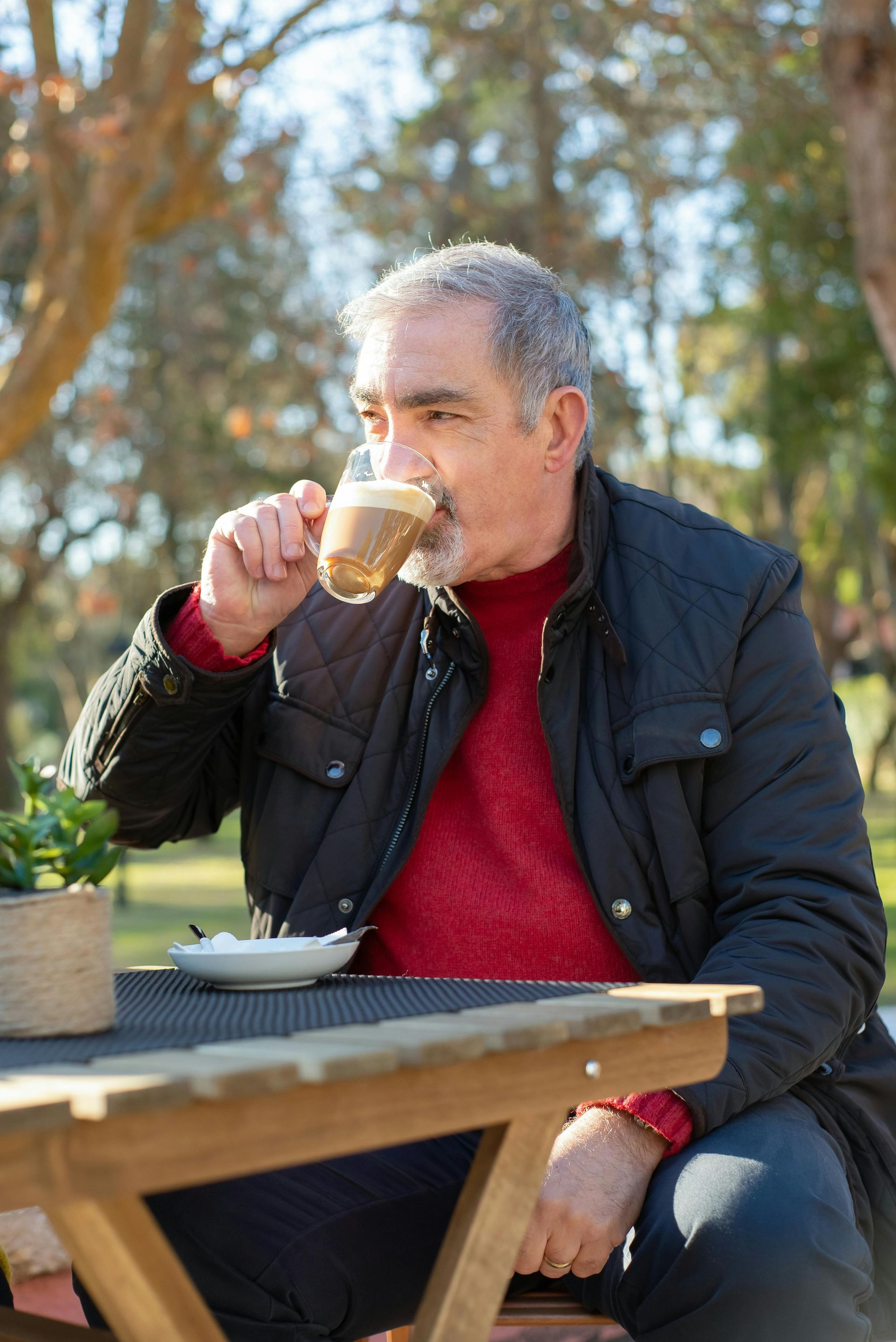 A man is sitting at a picnic table drinking a cup of coffee.