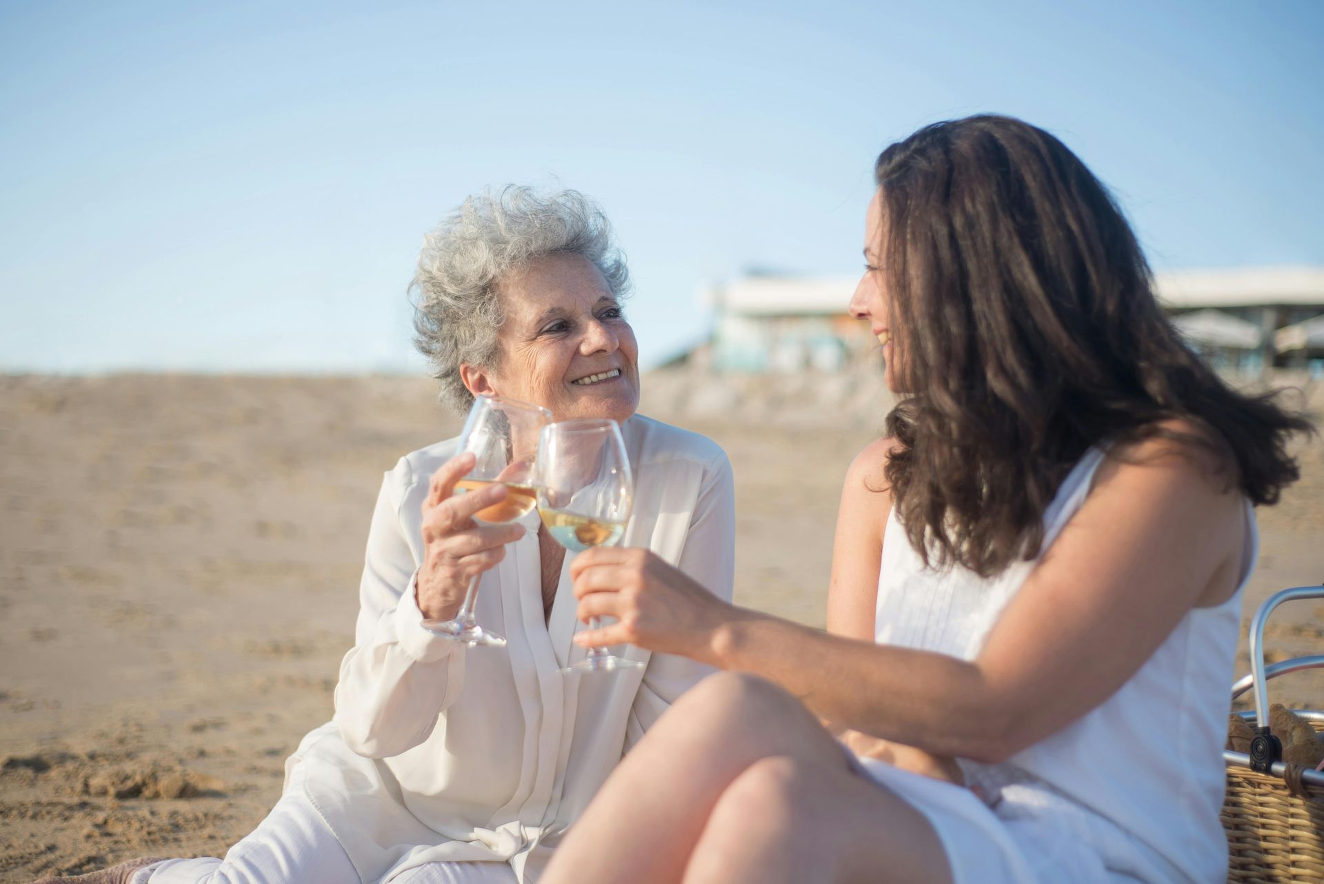 Two women are sitting on the beach drinking wine.