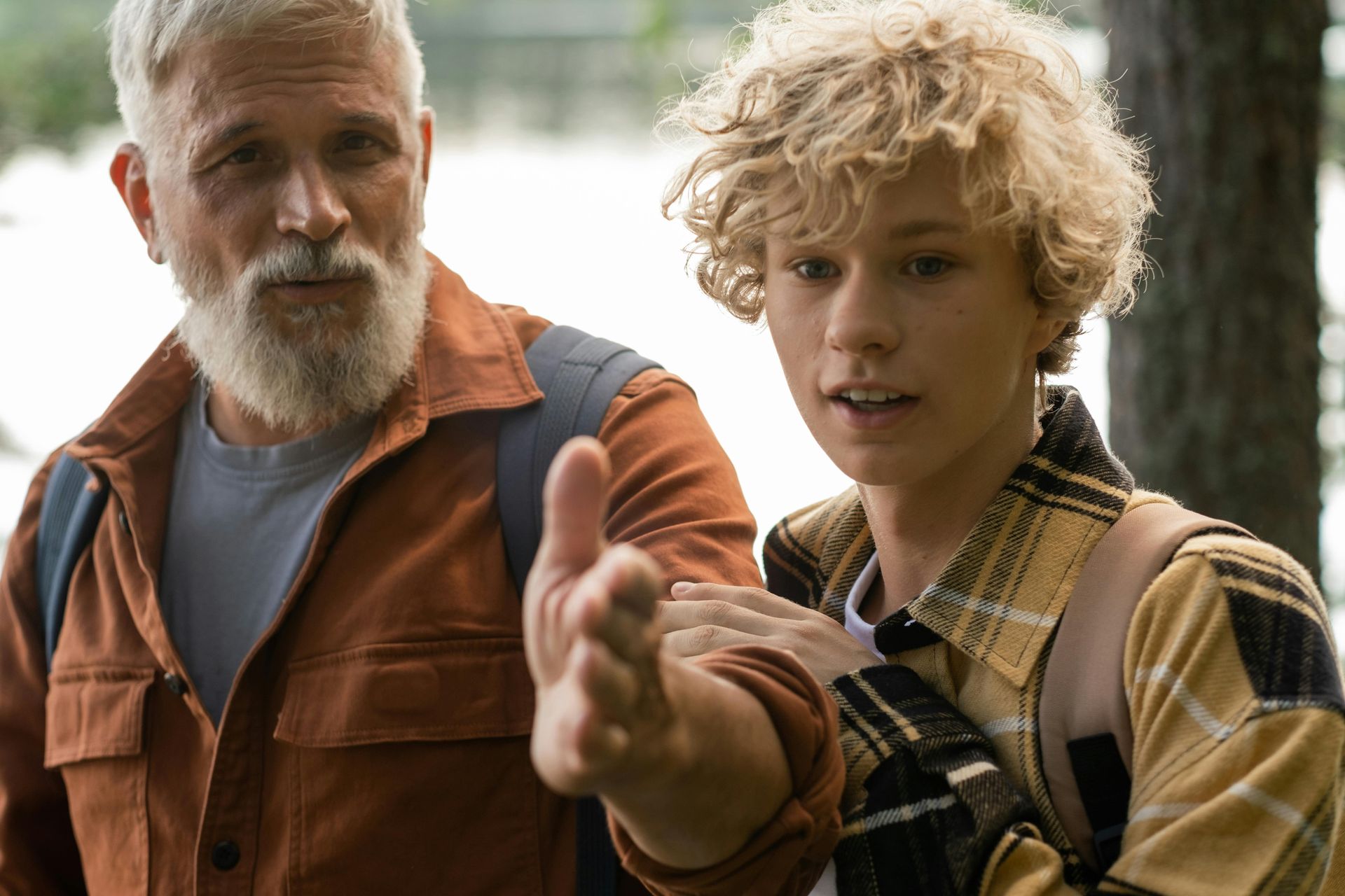 A man with a beard and a boy with curly hair are standing next to each other.