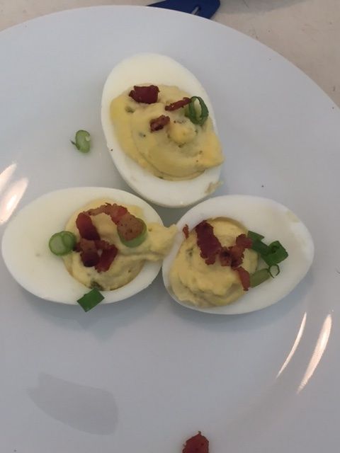 Three hard boiled eggs with bacon and green onions on a white plate