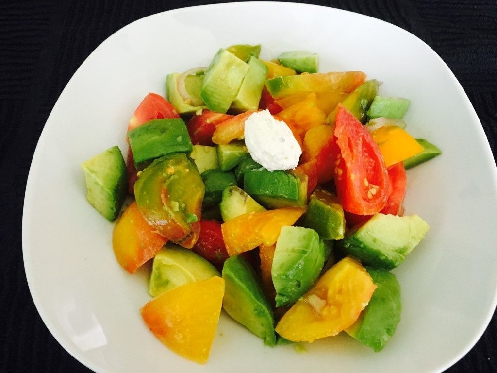A salad with avocado tomatoes and cucumbers on a white plate