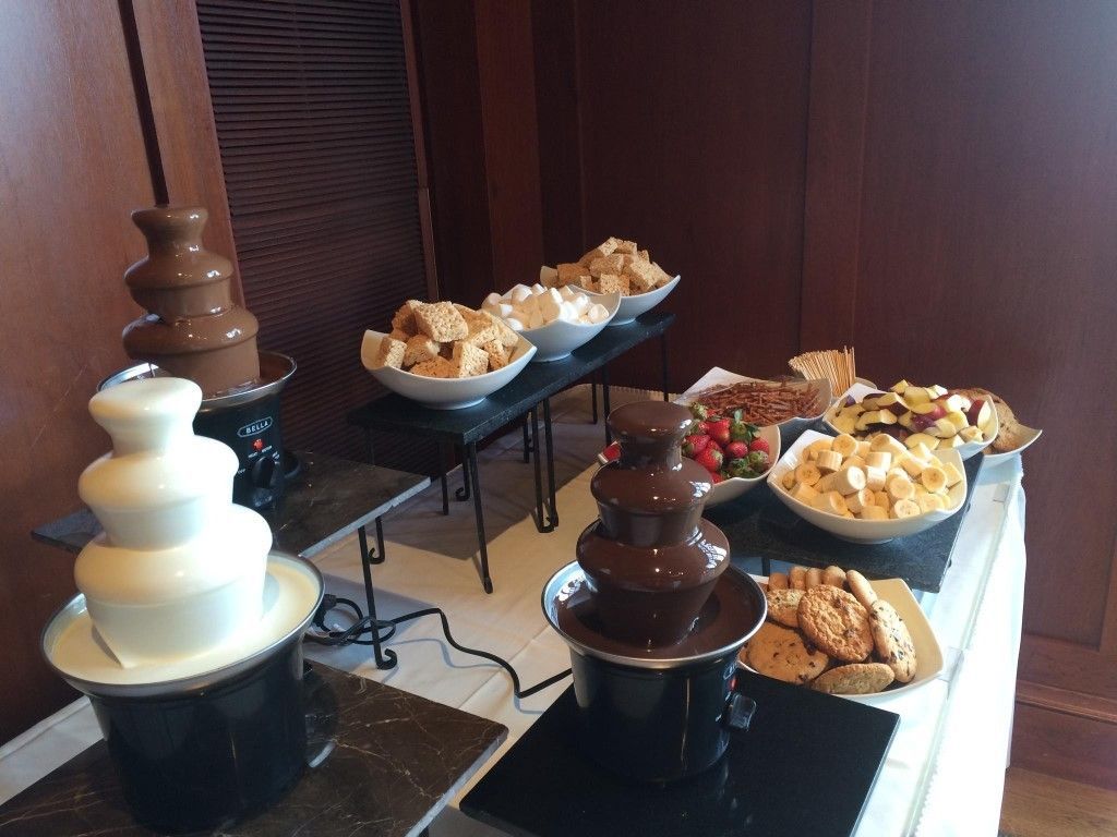 A table topped with chocolate fountains and a variety of snacks.