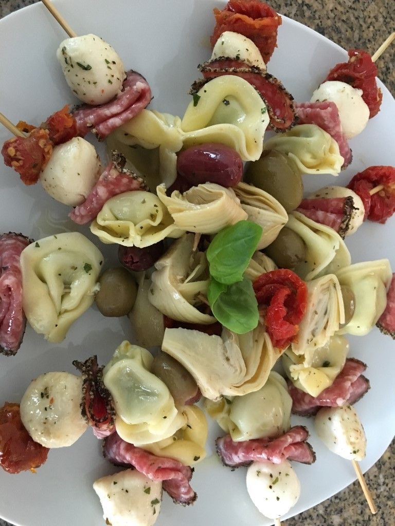 A white plate topped with a variety of food on skewers