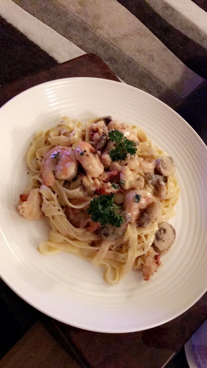 A plate of pasta with shrimp and mushrooms on a table.