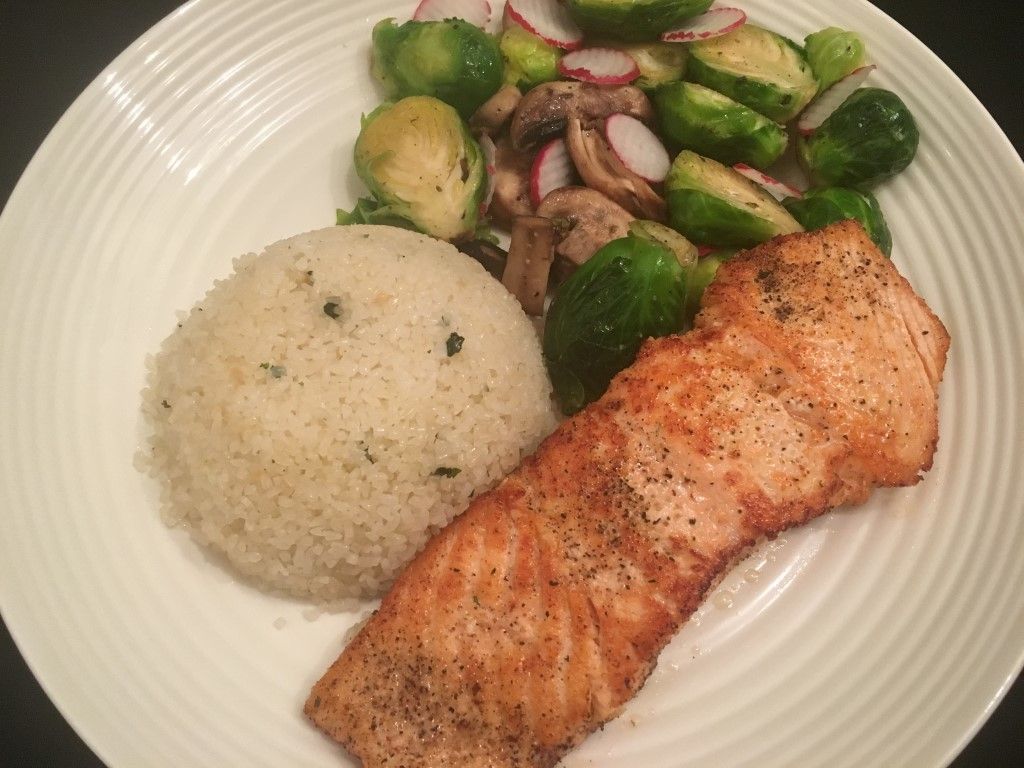A white plate topped with salmon rice and vegetables
