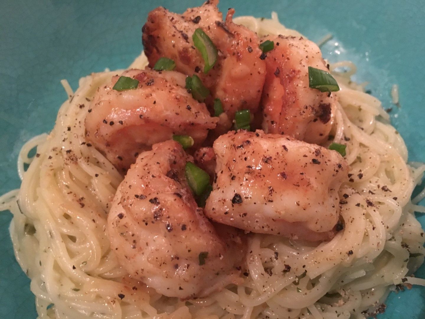A bowl of noodles with shrimp and green onions on top