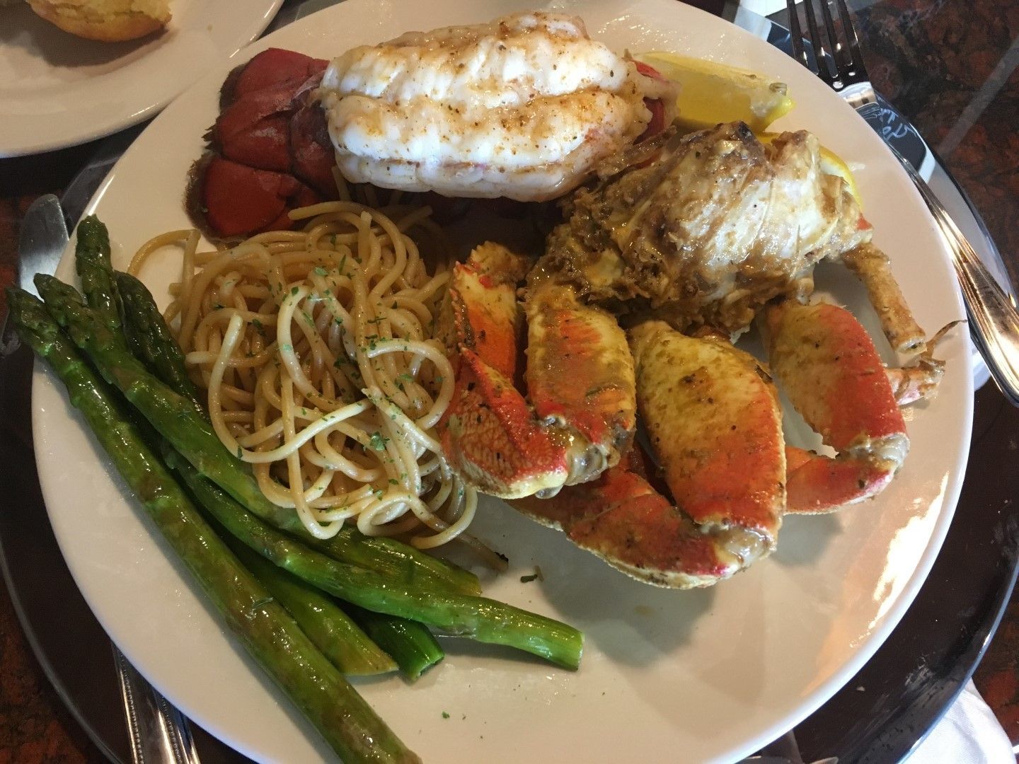 A white plate topped with lobster , asparagus , noodles and shrimp.