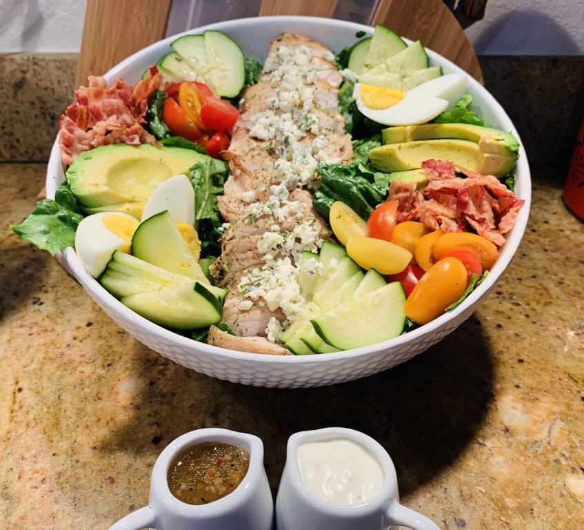 A salad in a bowl with two small pitchers of dressing next to it