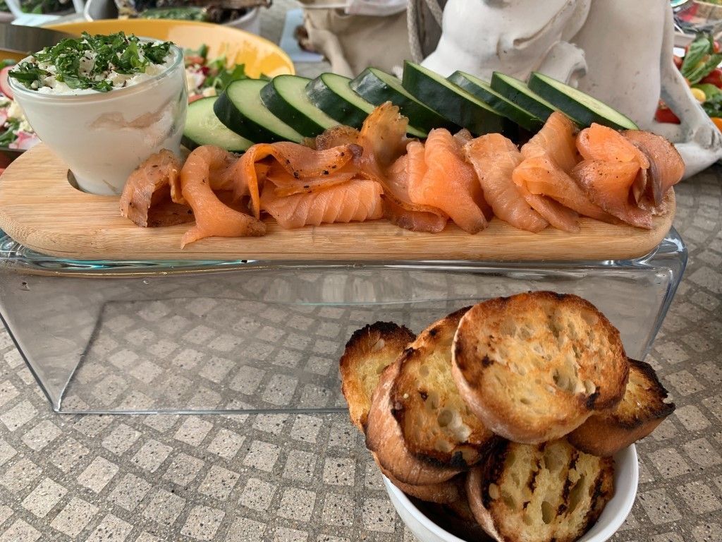 A wooden cutting board topped with smoked salmon and vegetables next to a bowl of croutons.