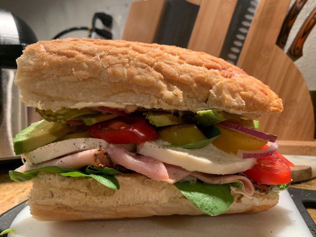 A sub sandwich with ham , cheese , tomatoes , onions and pickles on a cutting board.