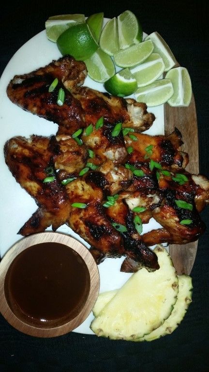 A white plate topped with grilled chicken wings pineapple and limes