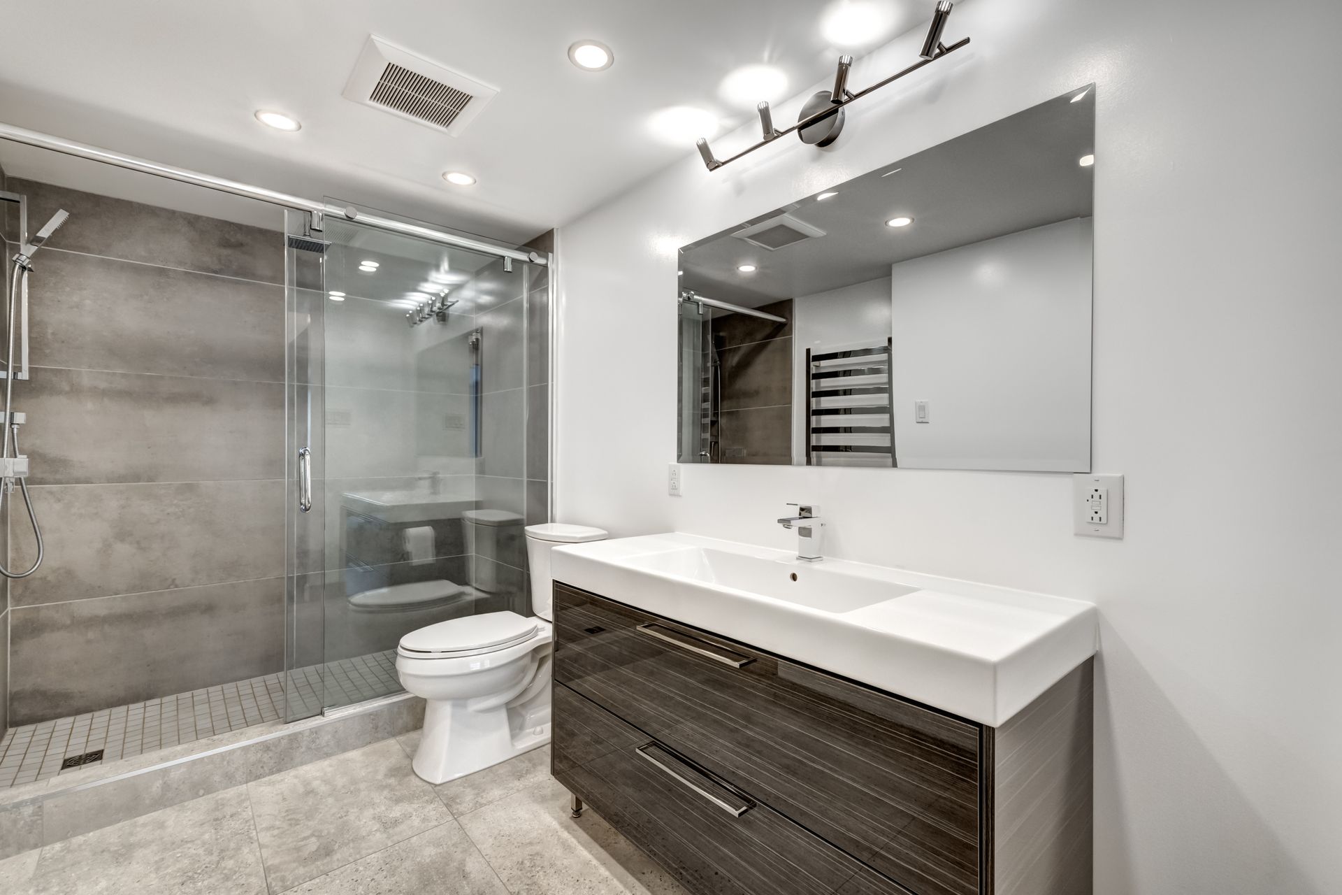 A modern bathroom with a glass-enclosed shower, a floating dark wood vanity, a white countertop, and a wide mirror.