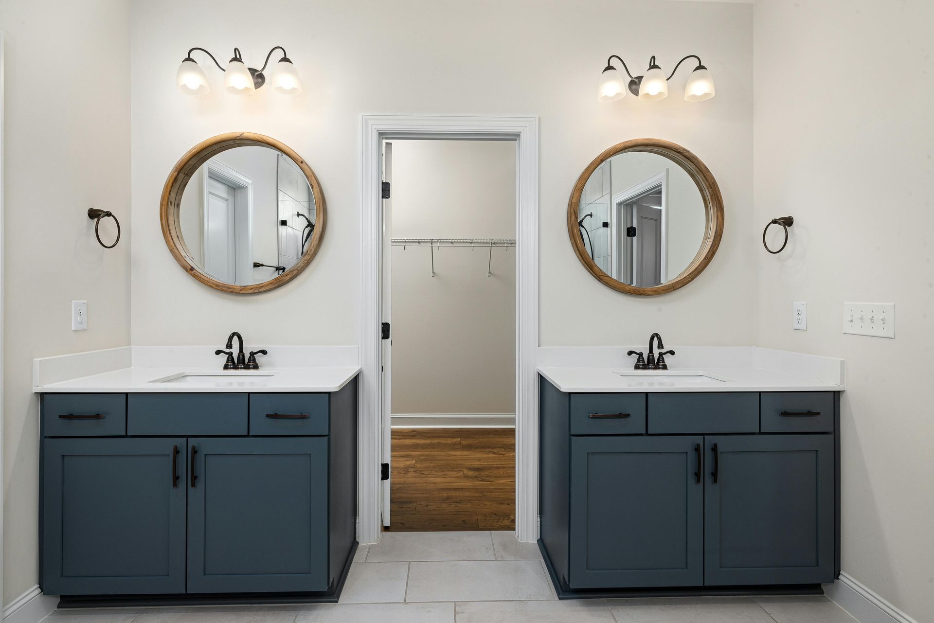 Modern bathroom with two blue vanities, round mirrors, and a central open closet door