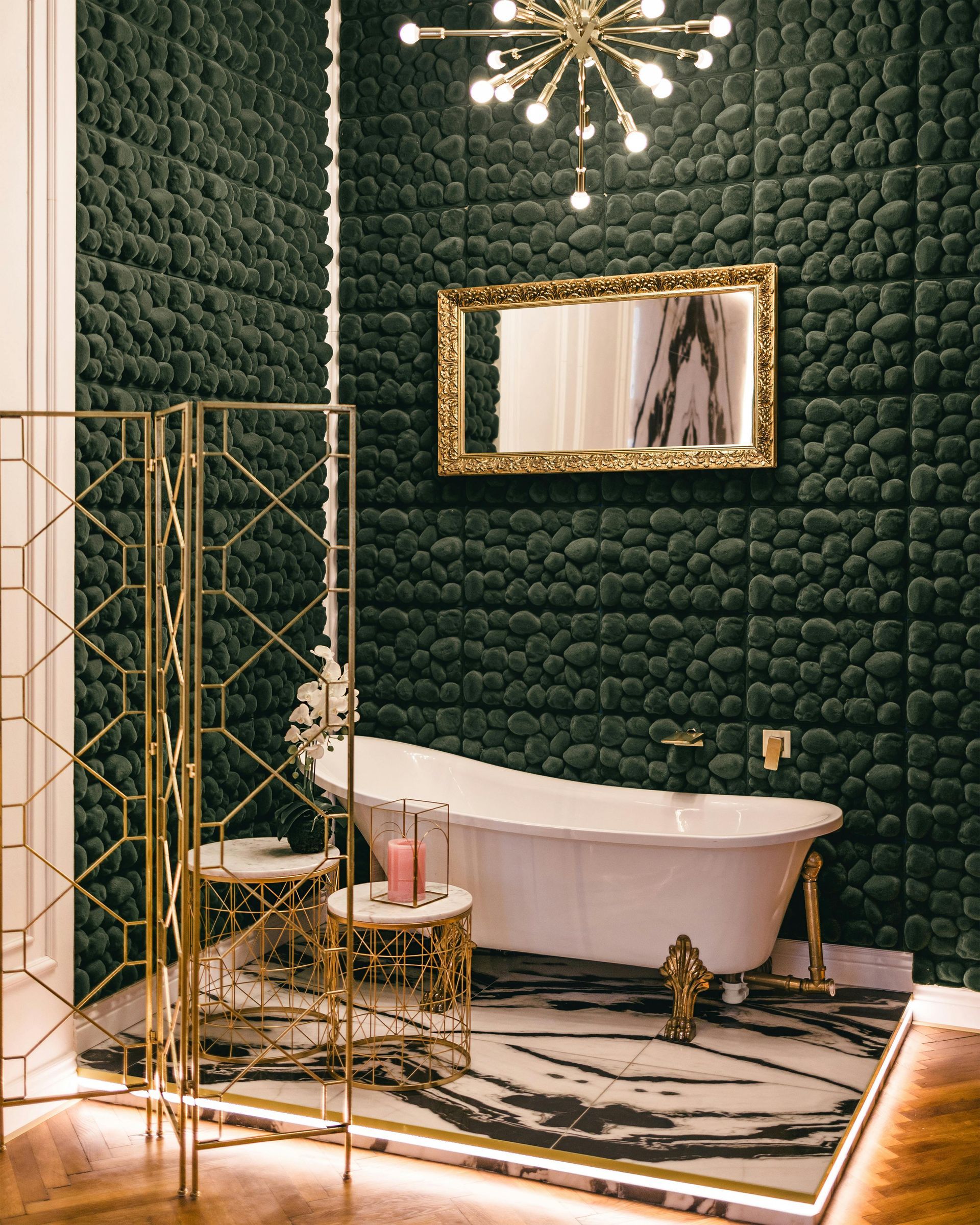 Elegant bathroom with dark green tiled walls, gold accents, a freestanding tub, and a modern chandelier.
