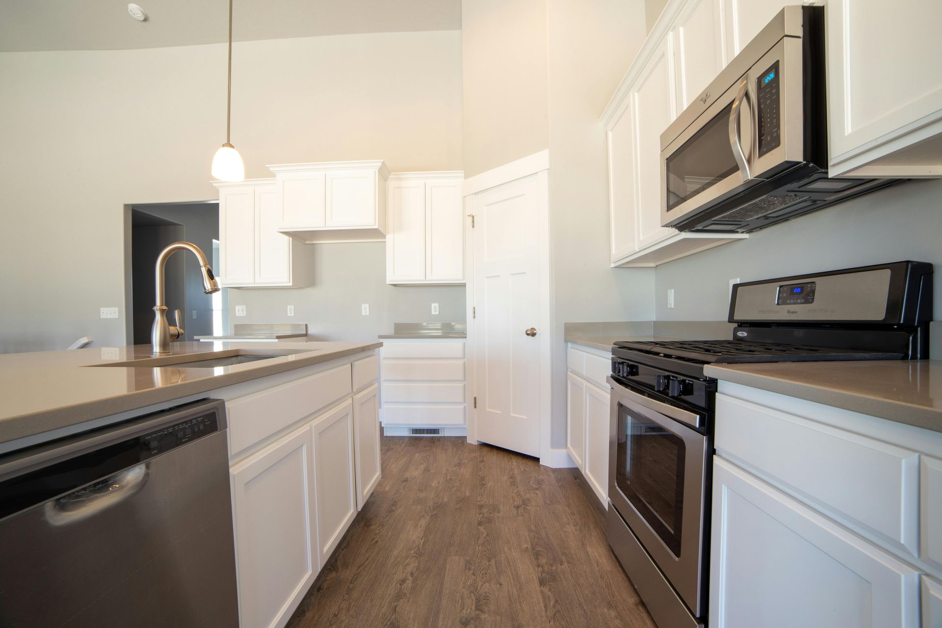Modern kitchen with white cabinets, stainless steel appliances, island sink, and wood flooring