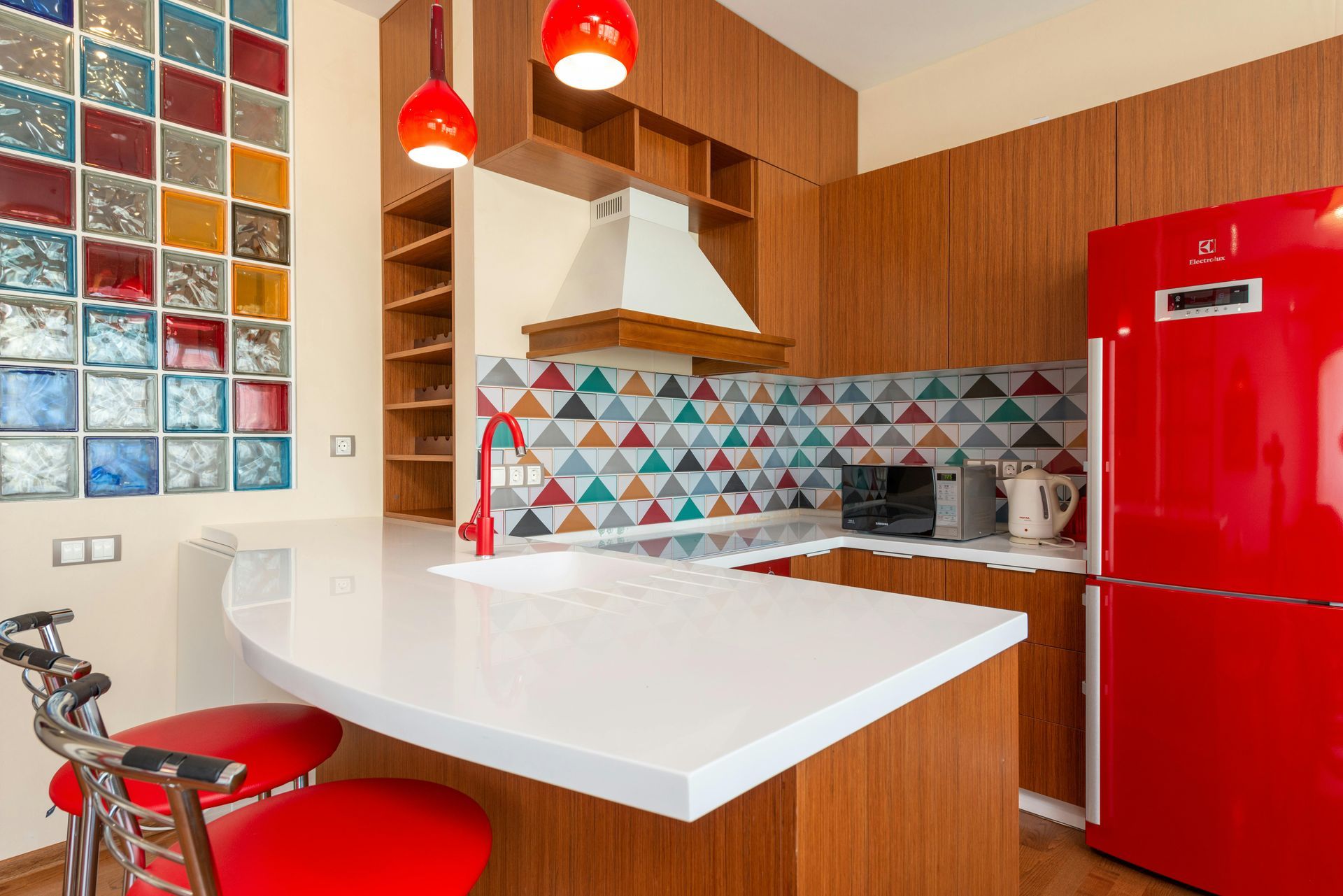 Modern kitchen with white island, red fridge, colorful tile backsplash, and hanging red lights