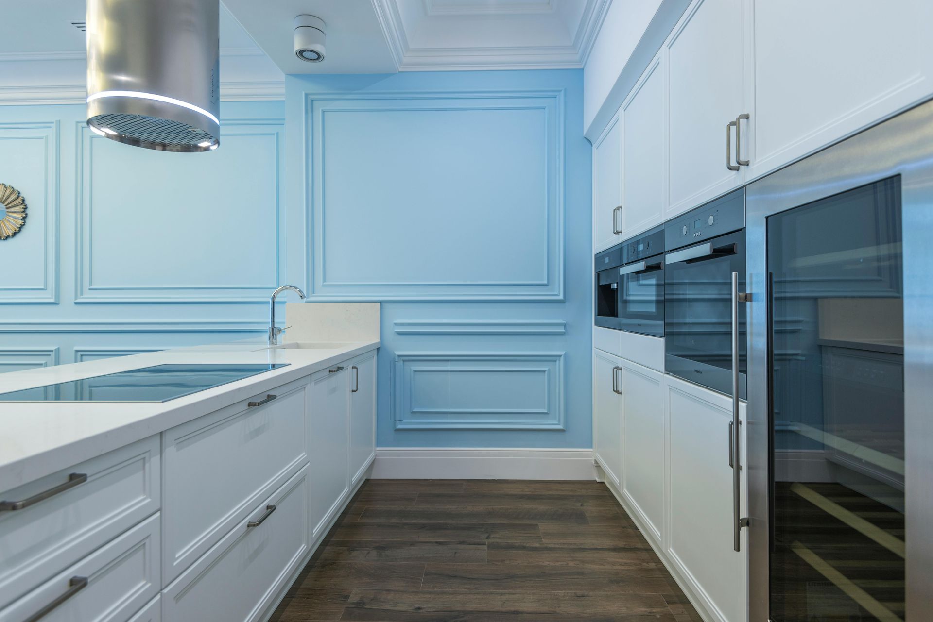 Bright blue and white modern kitchen with island, dark wood floor, and built-in ovens