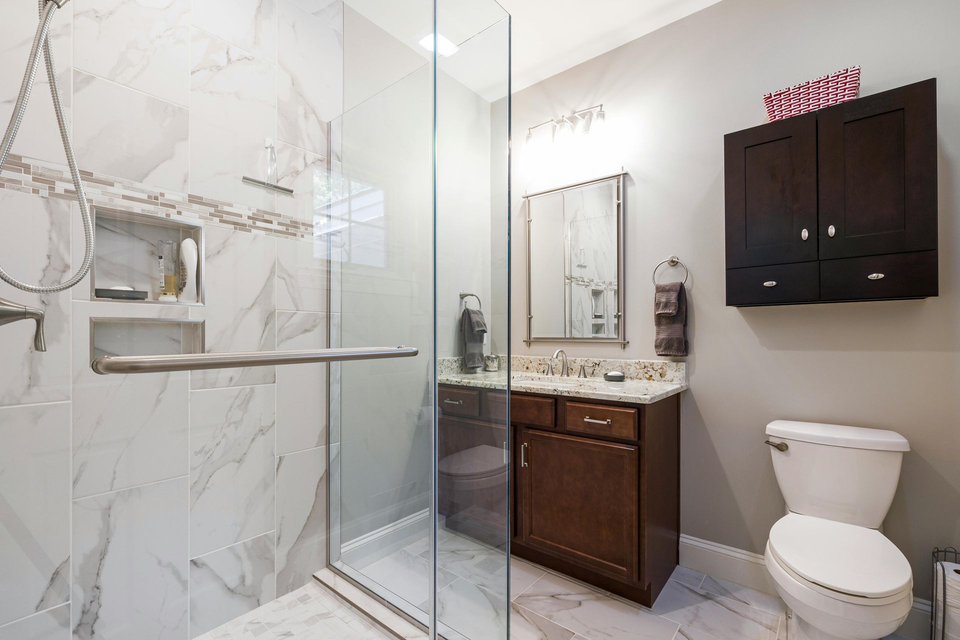 Modern bathroom with marble shower, dark vanity, mirror, towel rack, and toilet