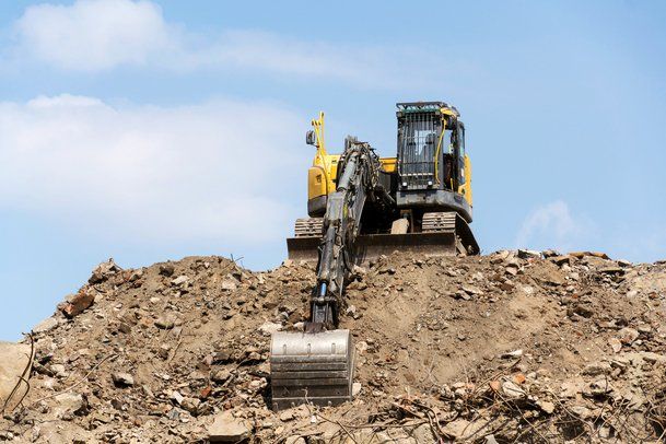 Picture of an excavator on top of a pile of debris.