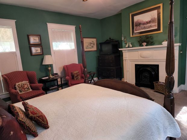 A bedroom with a four poster bed , chairs and a fireplace.