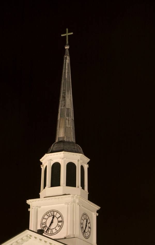A church steeple with a cross on top of it at night.