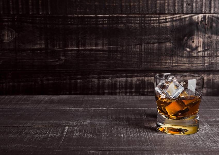A glass of whiskey with ice cubes on a wooden table.