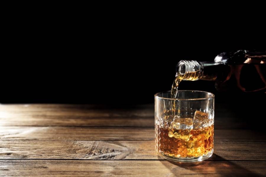 A glass of whiskey is being poured from a bottle on a wooden table.