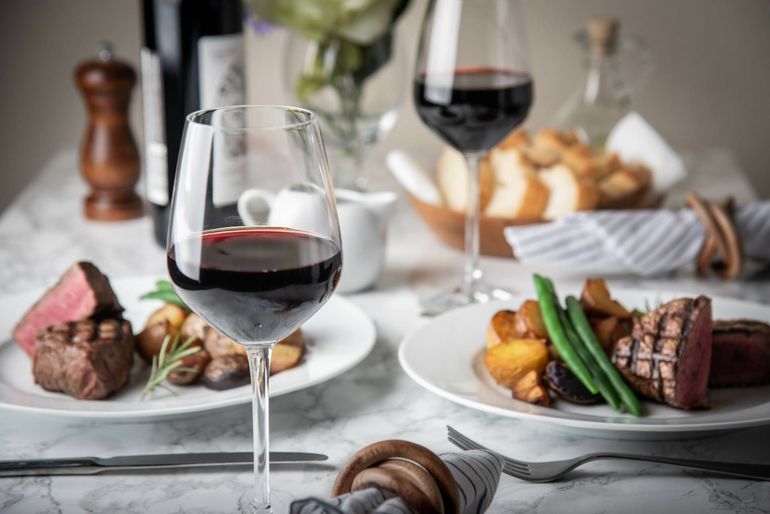 A table topped with plates of food and a glass of red wine.