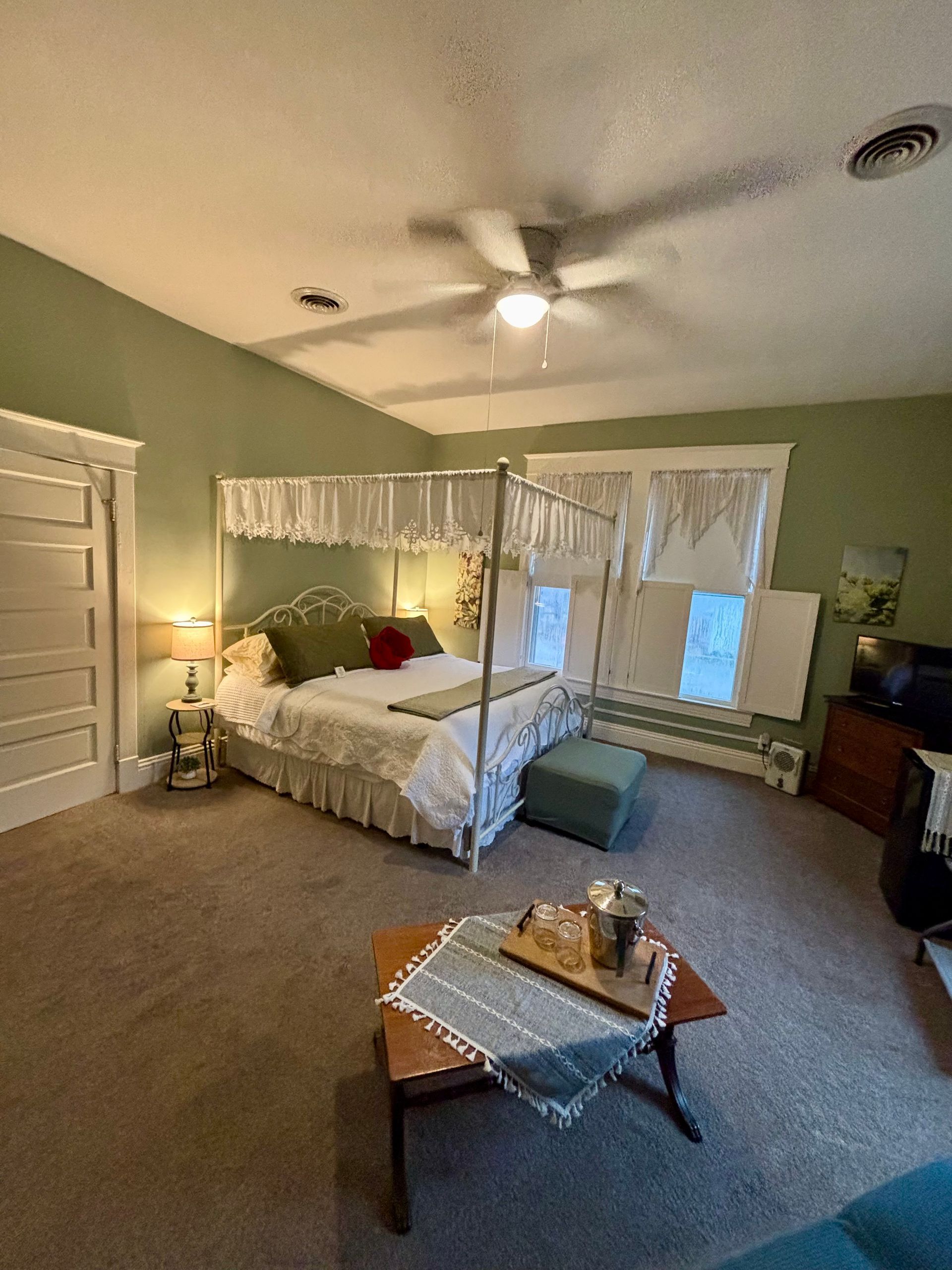 Bedroom with canopy bed, green walls, small table with food, and a window.
