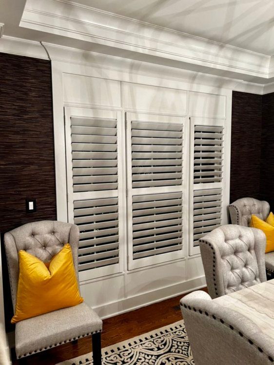 A living room with a couch , chairs , and shutters on the windows.