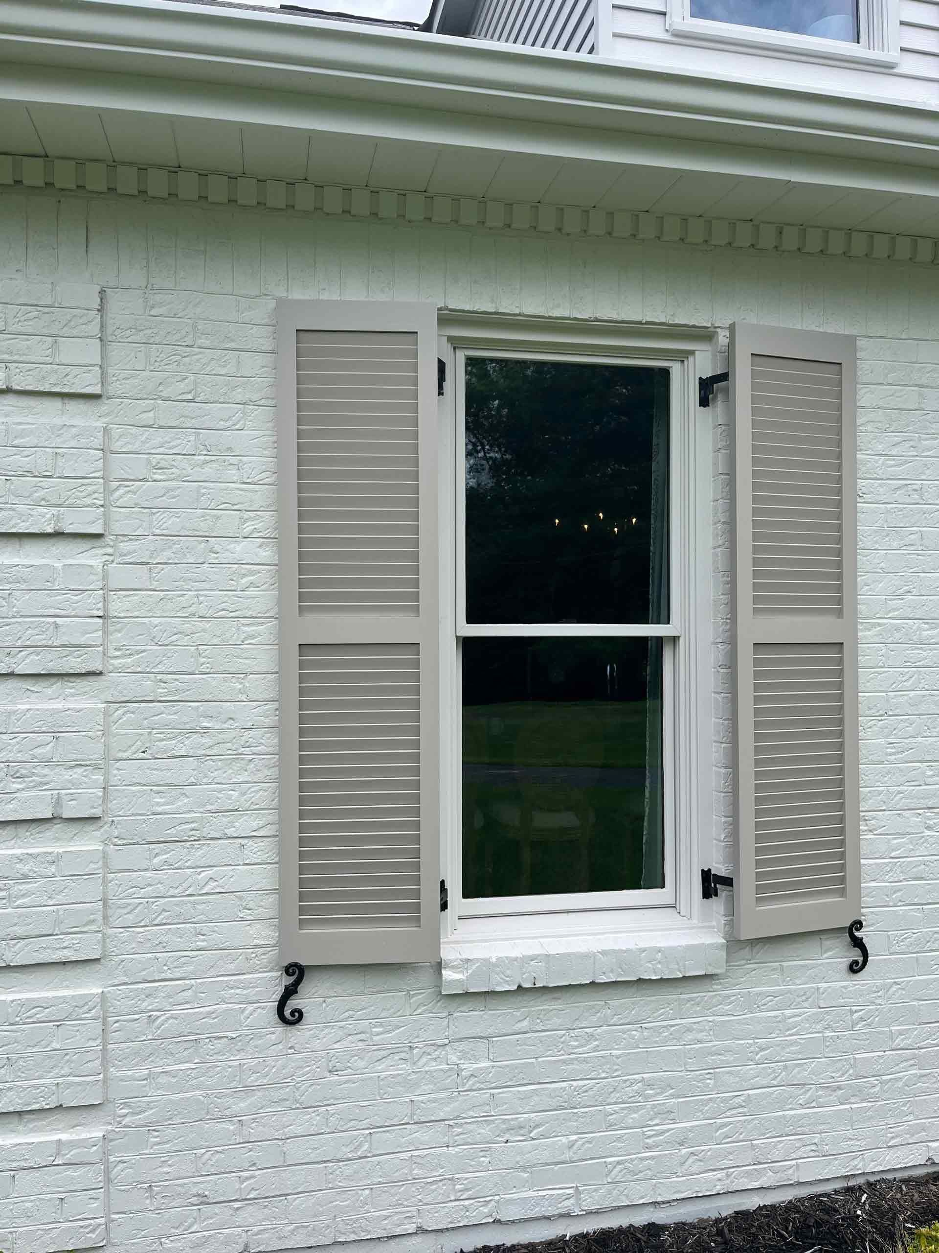 A white brick house with a window with shutters on it