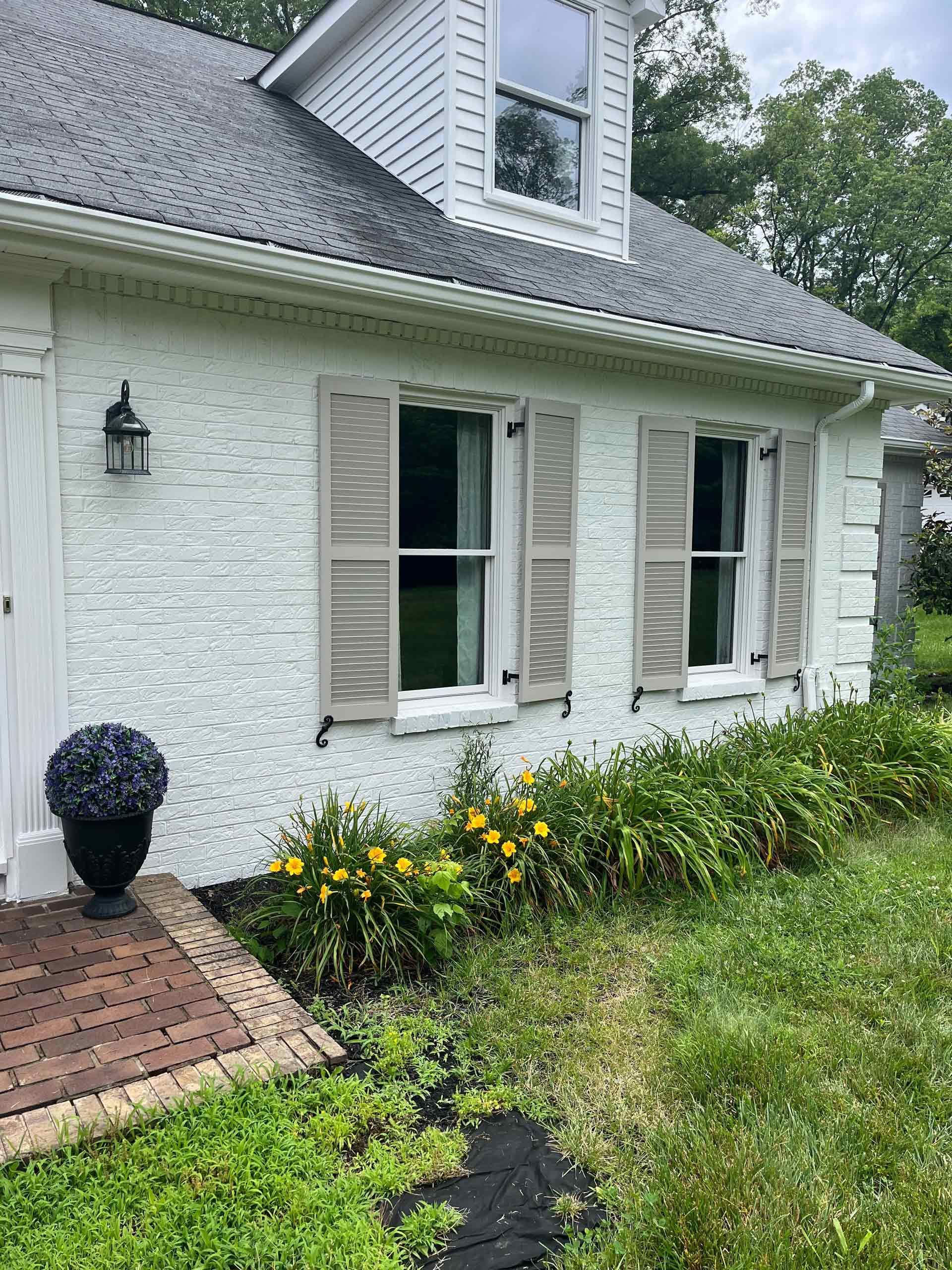 A white brick house with shutters on the windows and a brick porch.
