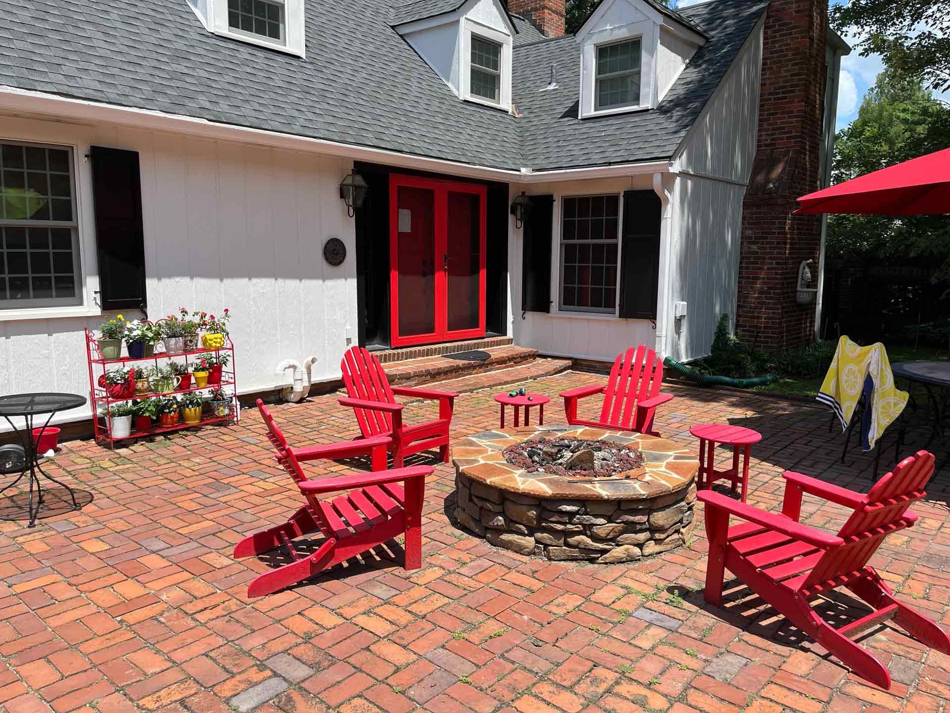 A patio with red chairs and a fire pit in front of a white house.