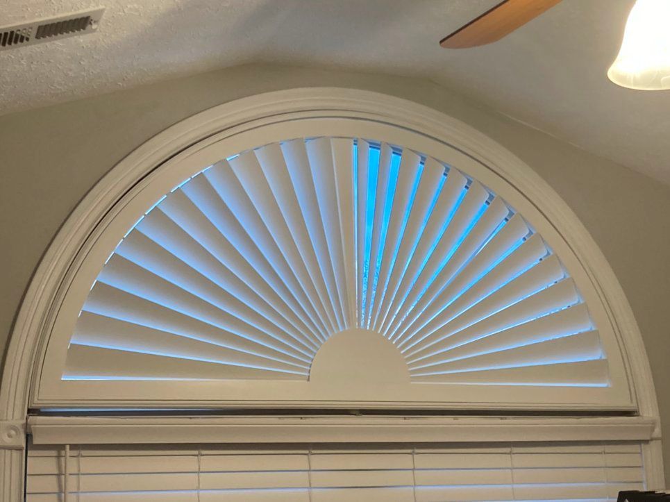 A window with arched blinds and a ceiling fan