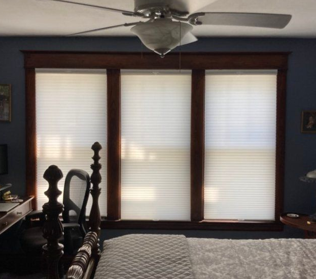 Bedroom with three windows framed in dark wood, white blinds, and a ceiling fan.