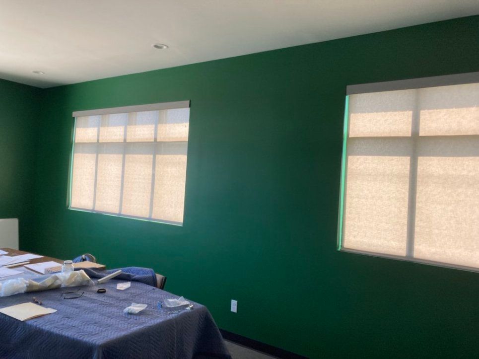 A room with green walls and white blinds on the windows.
