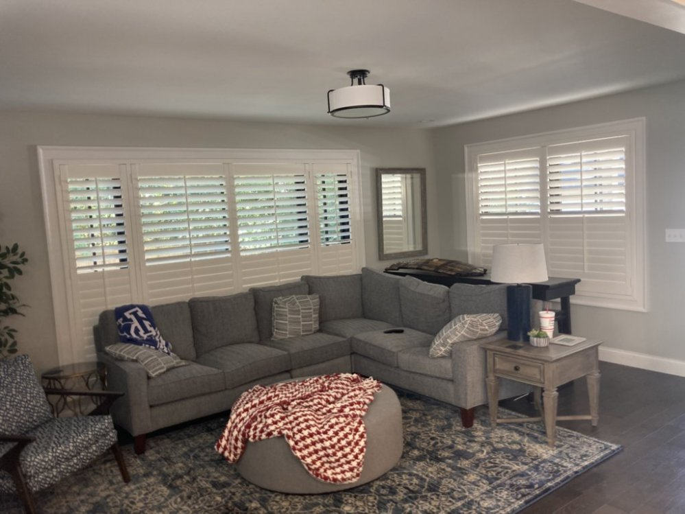 A living room with a sectional couch , ottoman , table and mirror.