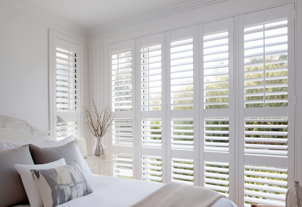 Bedroom with white shutters, bed with gray pillows and white comforter.