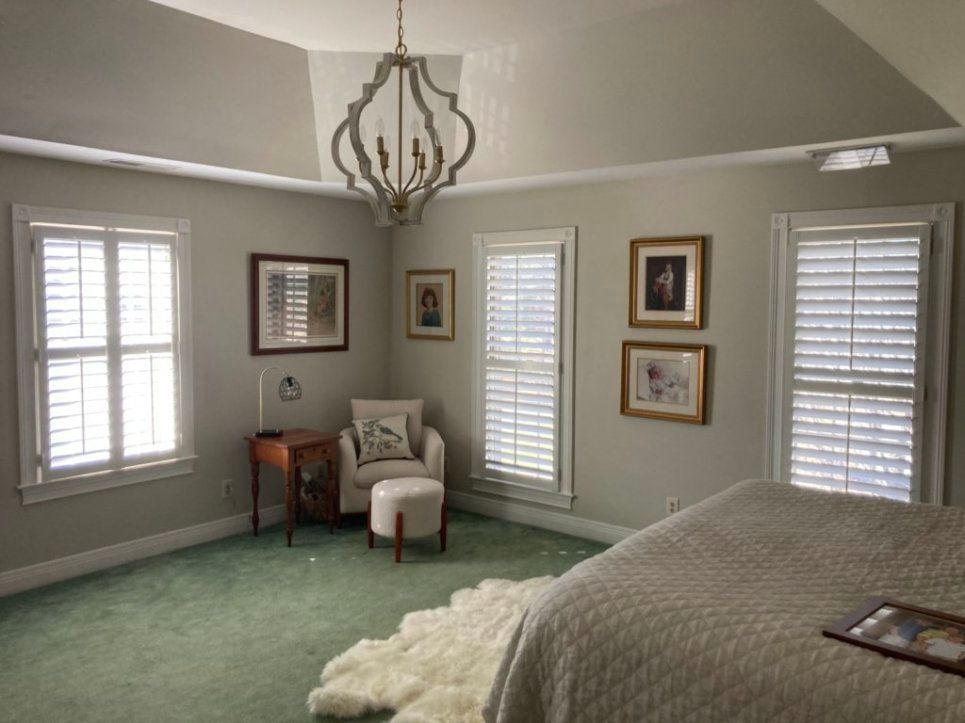 A bedroom with a bed , chair , table and window shutters.