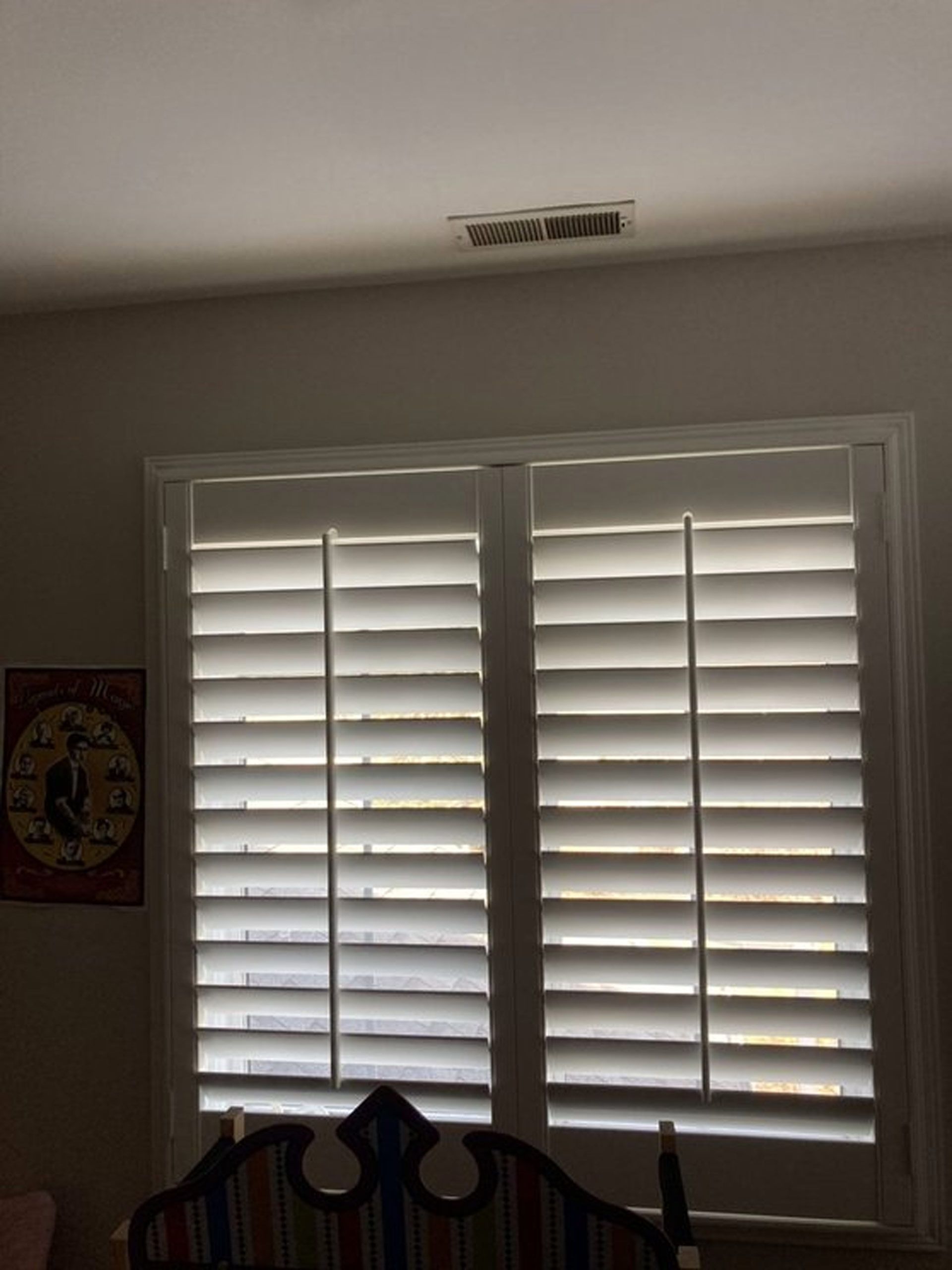 A bedroom with white shutters on the windows and a clock on the wall.