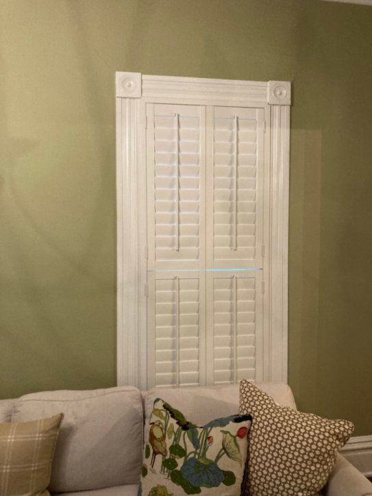 A living room with a couch and pillows and a window with shutters