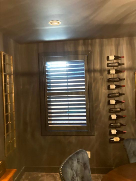 A room with a window and a row of wine bottles hanging on the wall.