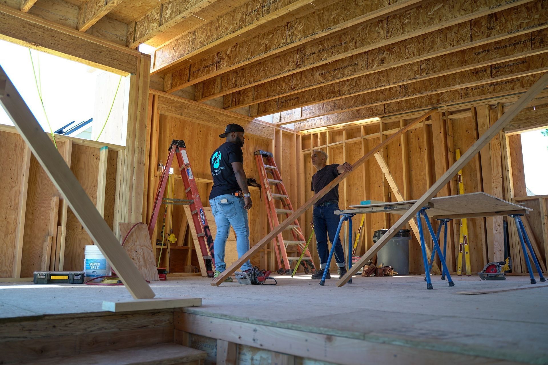 Two men are working on a wooden structure and one has a t-shirt that says ' a ' on it