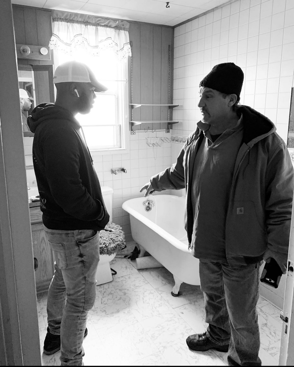 Two men are standing in a bathroom next to a bathtub.