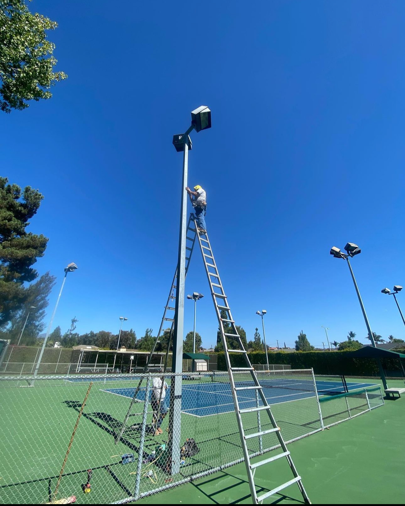 A man on a ladder is working on a tennis court
