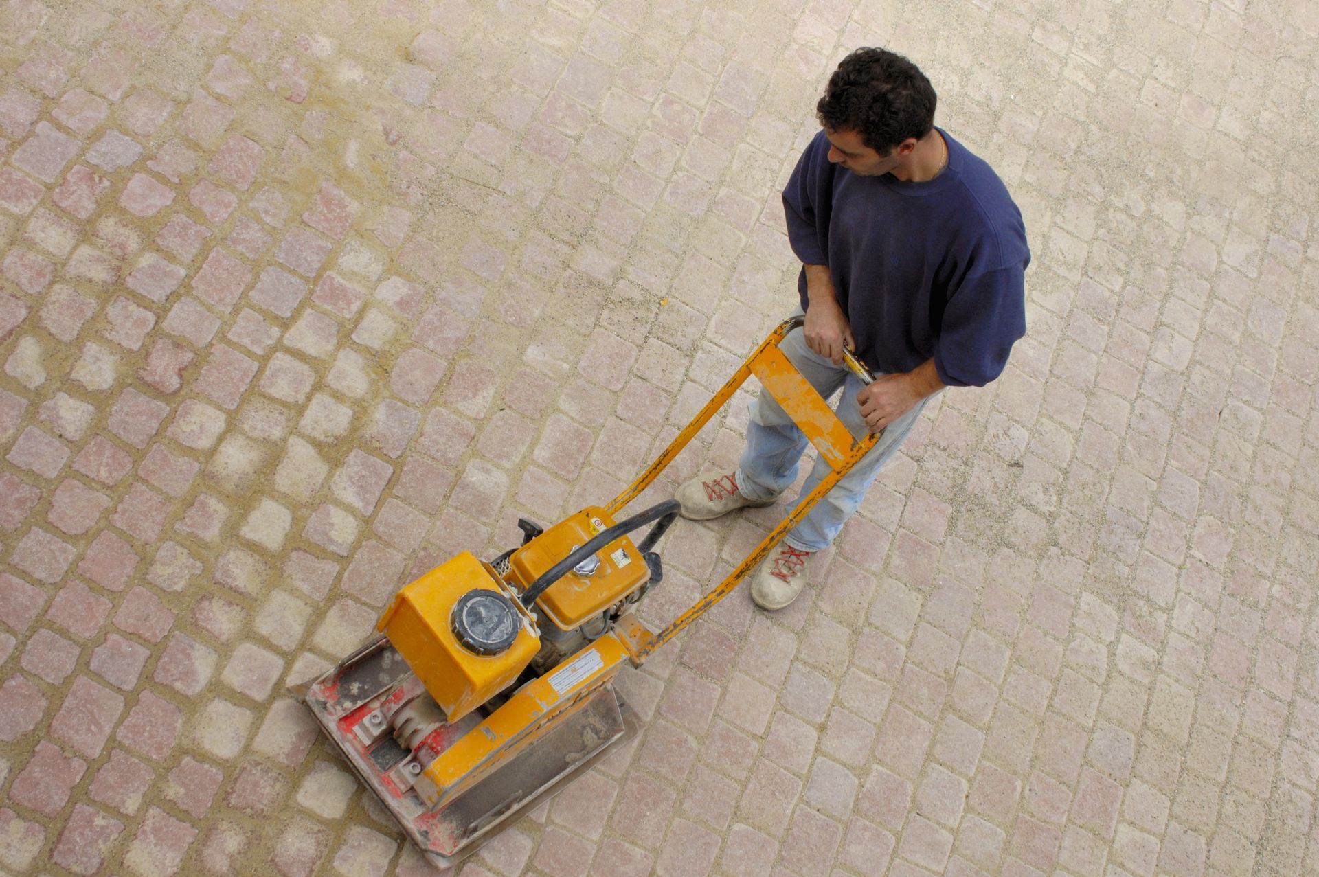 A man is using a machine on a brick pavement