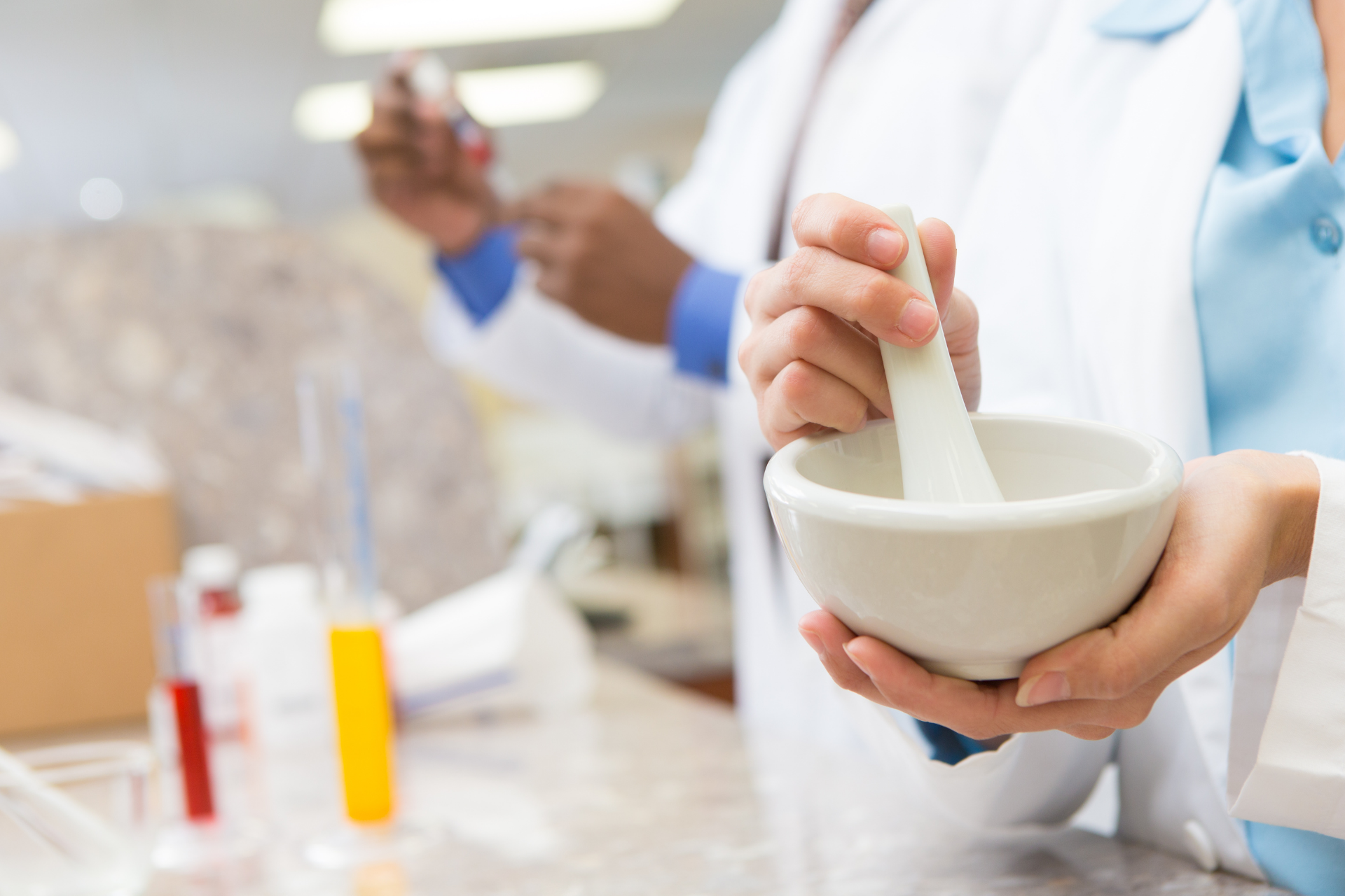 Lab technicians grinding a sample in a mortar and pestle in a bright laboratory