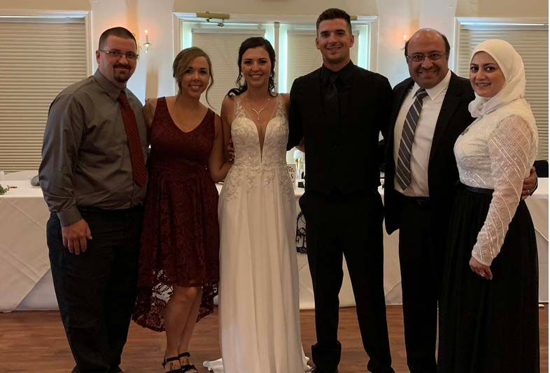 Six people dressed formally pose together at a wedding reception.