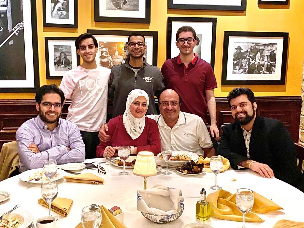 Group of six smiling people seated at a restaurant table with framed artwork on the wall behind them.