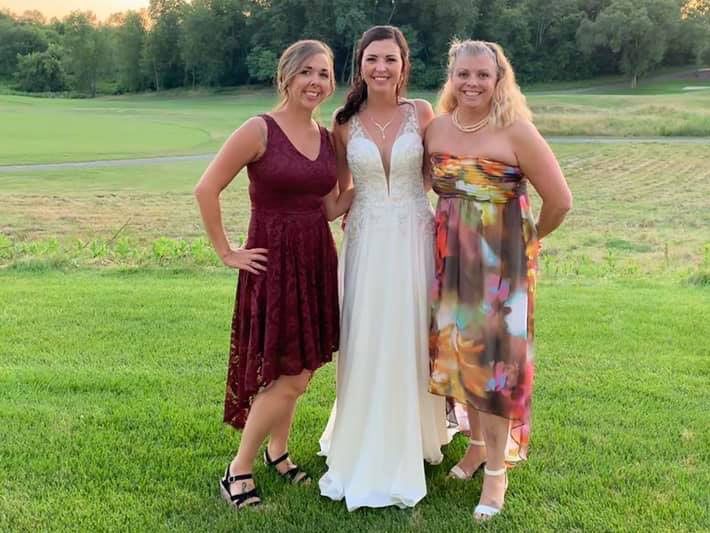Three women in dresses posing on a grassy field at sunset